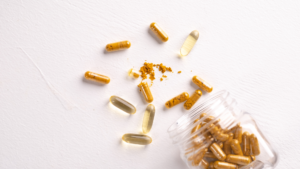 Assorted capsule sizes spilled from a jar next to loose powder and softgels