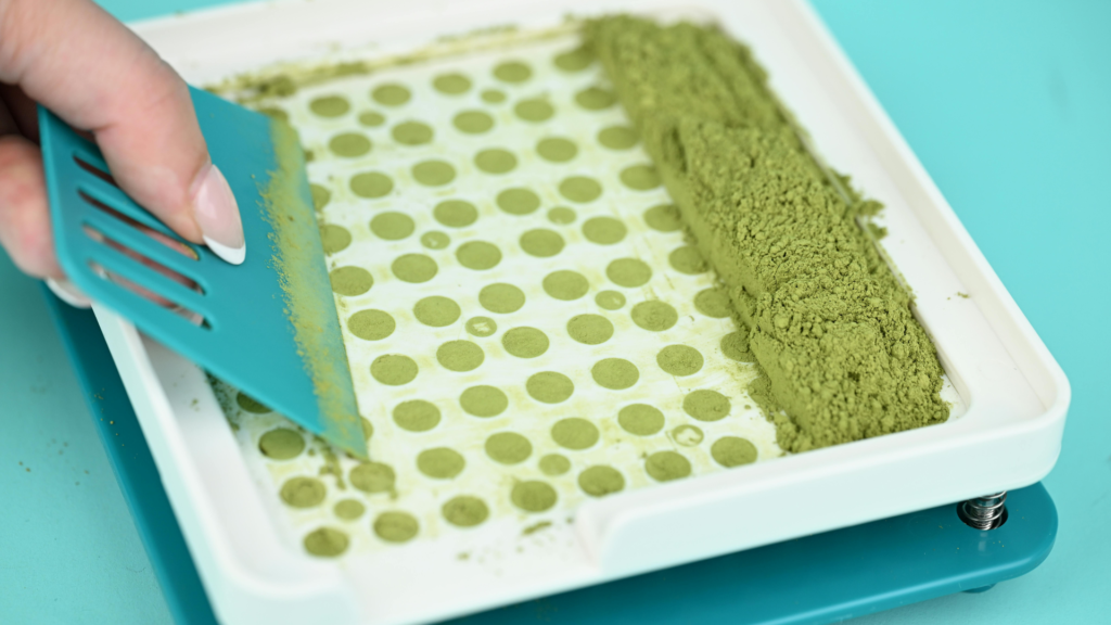 Hand leveling powder into a capsule tray, demonstrating how to fill capsules by hand