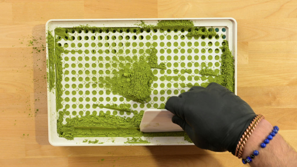 Hand spreading powder across a capsule filling machine plate before tamping