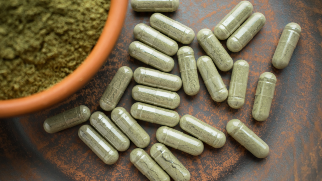 Kratom powder and filled capsules next to a capsule filling machine setup