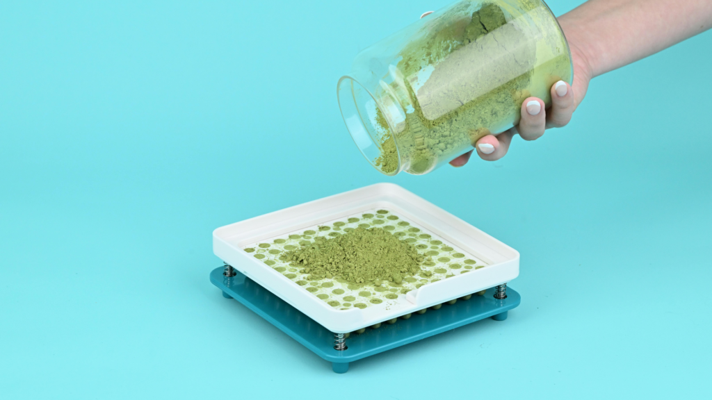 Powder being poured onto a capsule filling machine tray for batch loading