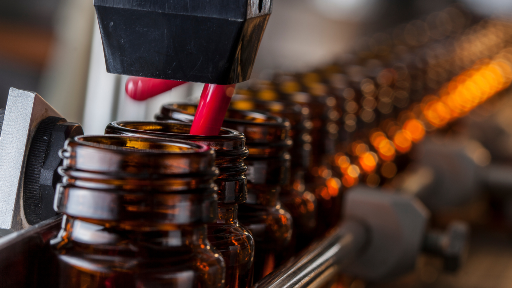Automated filling machine dispensing liquid into amber bottles on a production line.