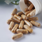 Capsules spilled out of a white bottle next to green leaves.