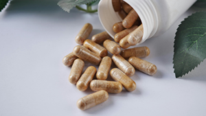 Capsules spilled out of a white bottle next to green leaves.