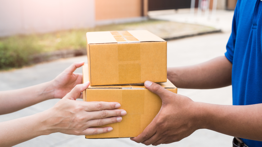 Delivery person handing cardboard packages to a customer at the door.