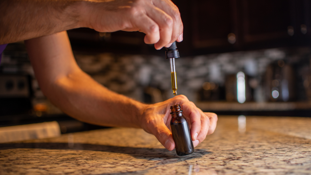 Hand using a dropper to measure liquid for filling capsules with oil.