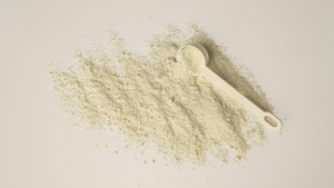 Measuring scoop of powder next to a spread of loose powder on a white background