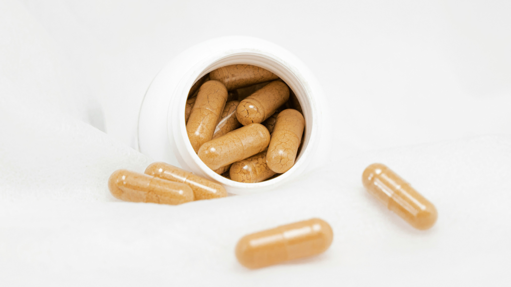 Open supplement bottle with powder-filled capsules spilling out onto a white surface
