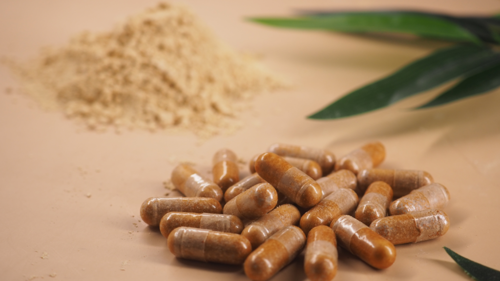 Vegan capsules next to herbal powder and a green plant leaf